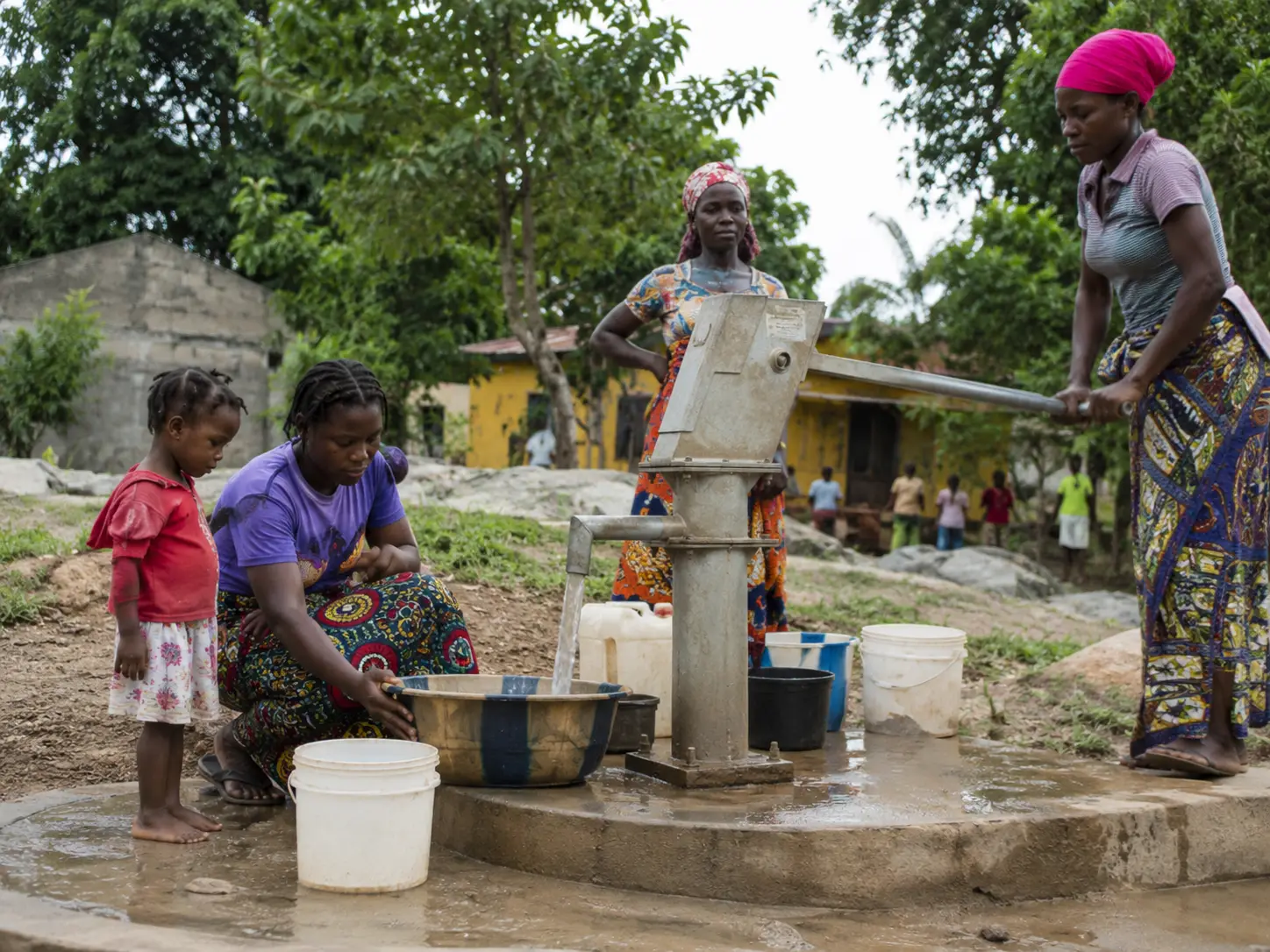 Women and children collecting safe drinking water from a local hand pump in Liberia